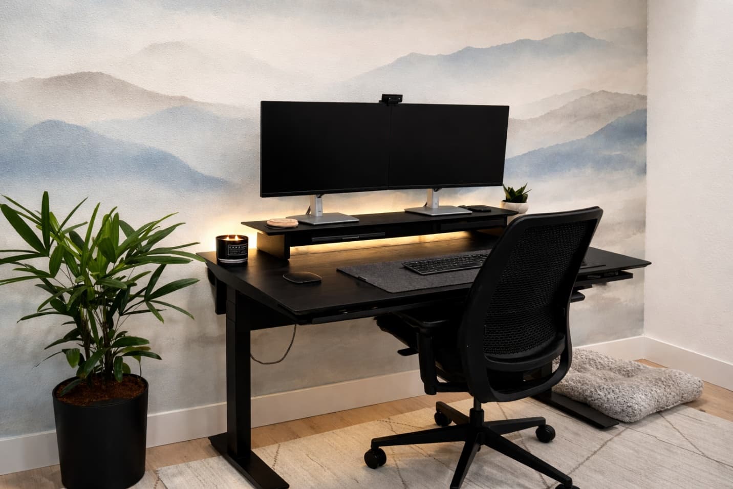 Modern home office with sleek black desk setup against soft misty mountain wallpaper