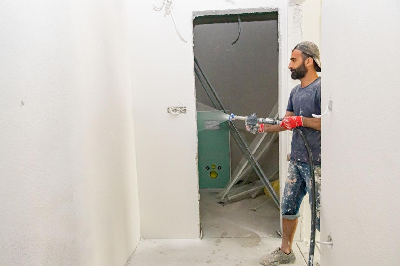 Spraying a smoothing coat onto a rough wall surface